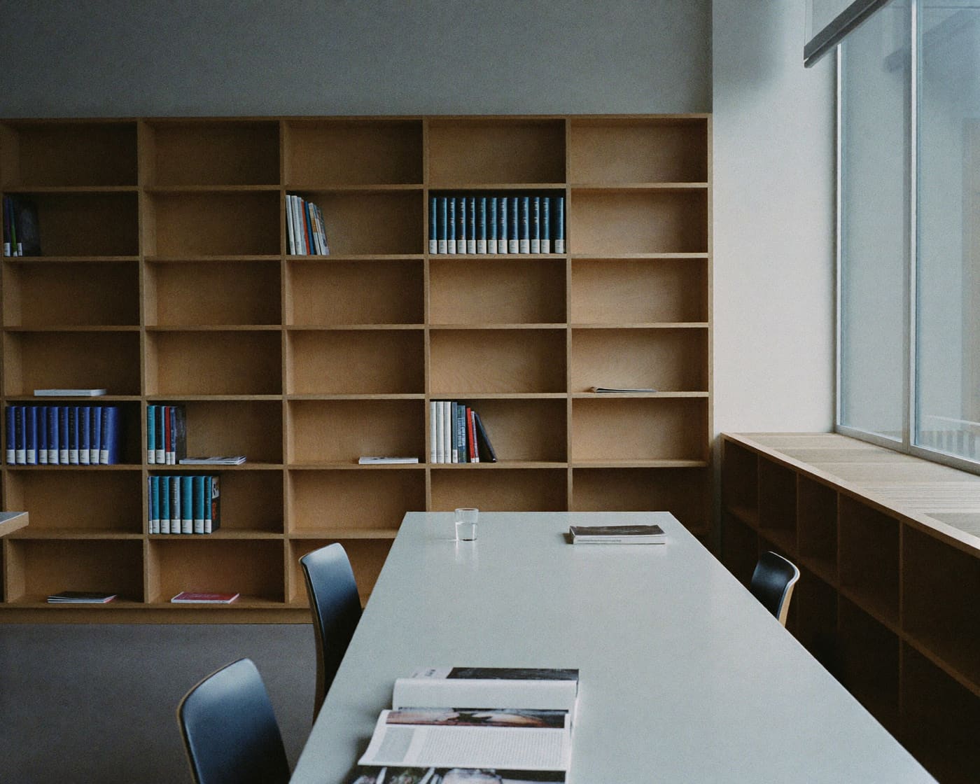 Minimal research library with pale oak shelving in soft morning light
